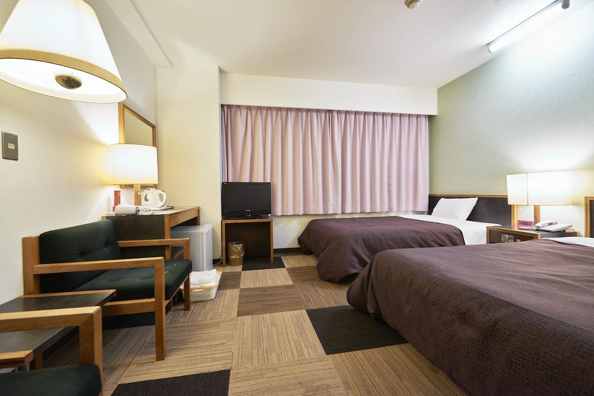 A hotel room with two beds, a desk with a chair, a television, and a window with curtains.