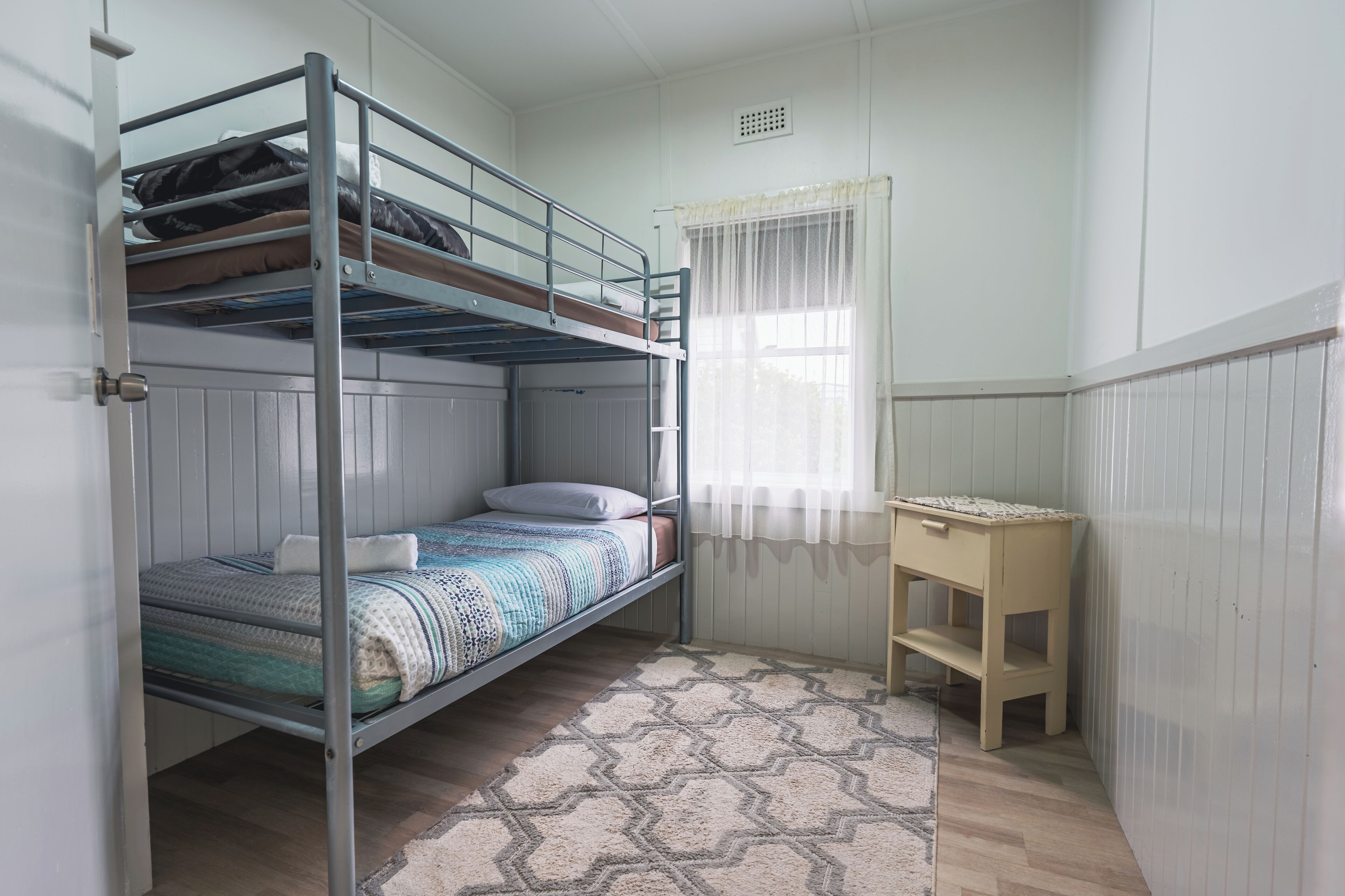 A bunk bed room with a desk and a window with sheer curtains.