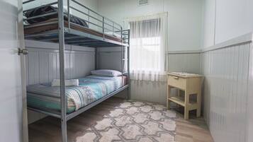 A bunk bed room with a desk and a window with sheer curtains.