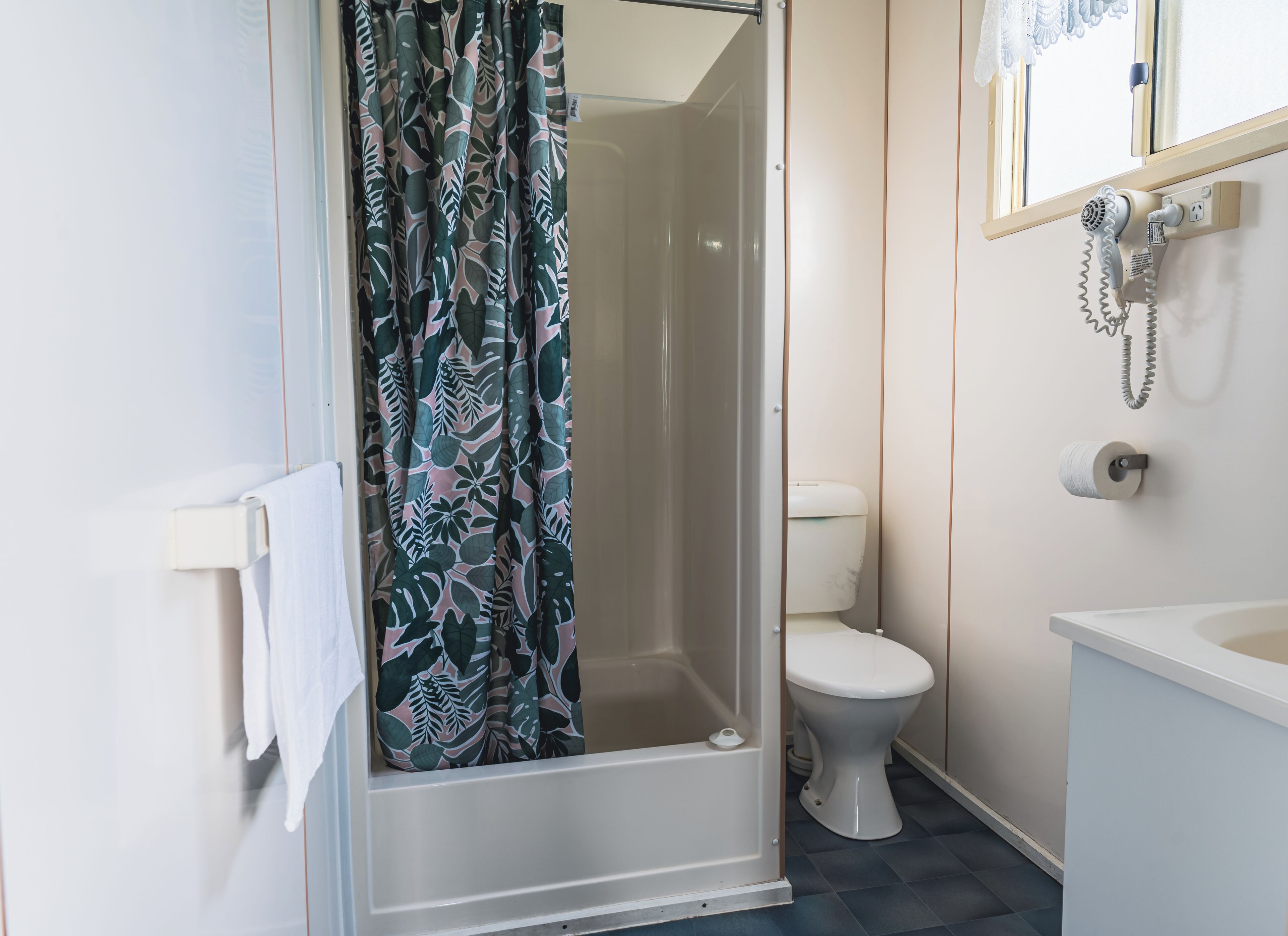 A bathroom with a shower, toilet, and a hairdryer mounted on the wall.