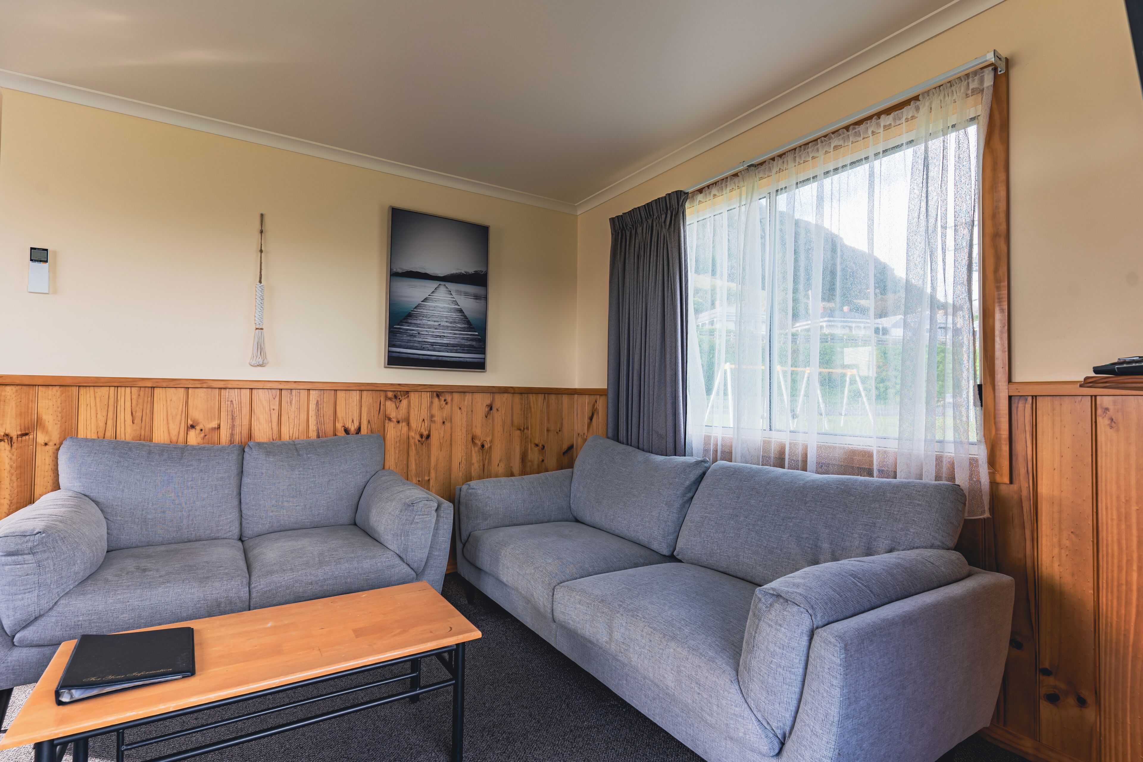 A room with two grey sofas, a wooden table, and a window with sheer curtains.