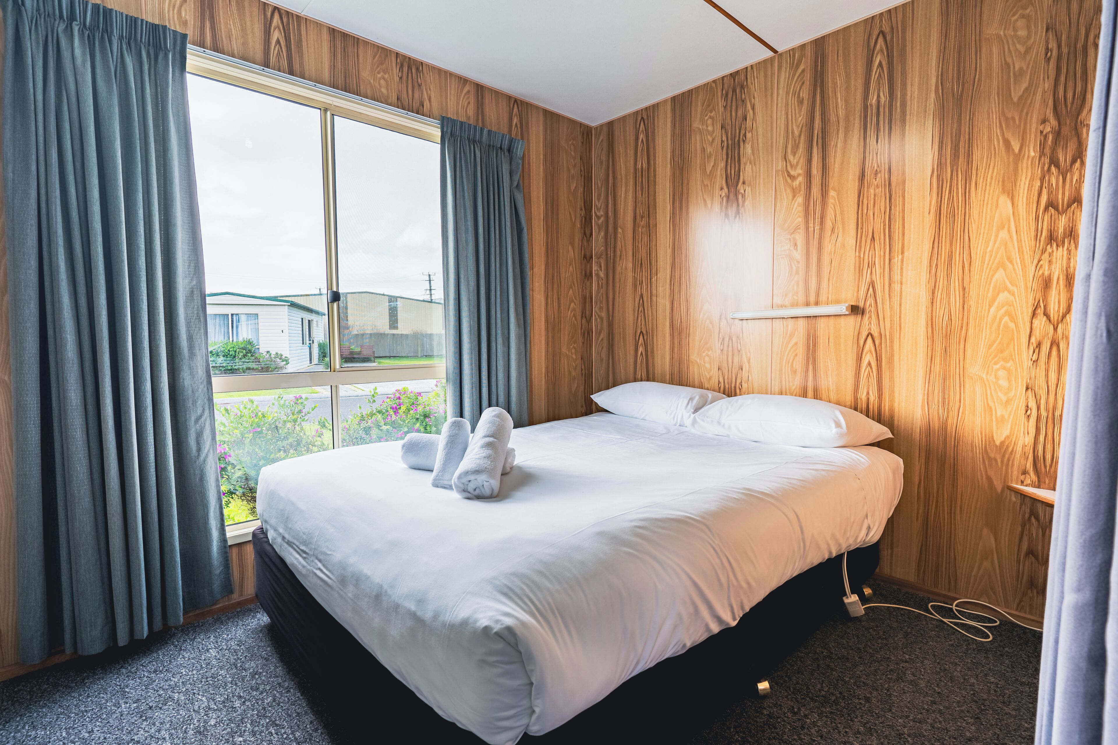 Habitación de hotel con una cama grande, paneles de madera, una ventana con cortinas y vistas a zonas verdes.