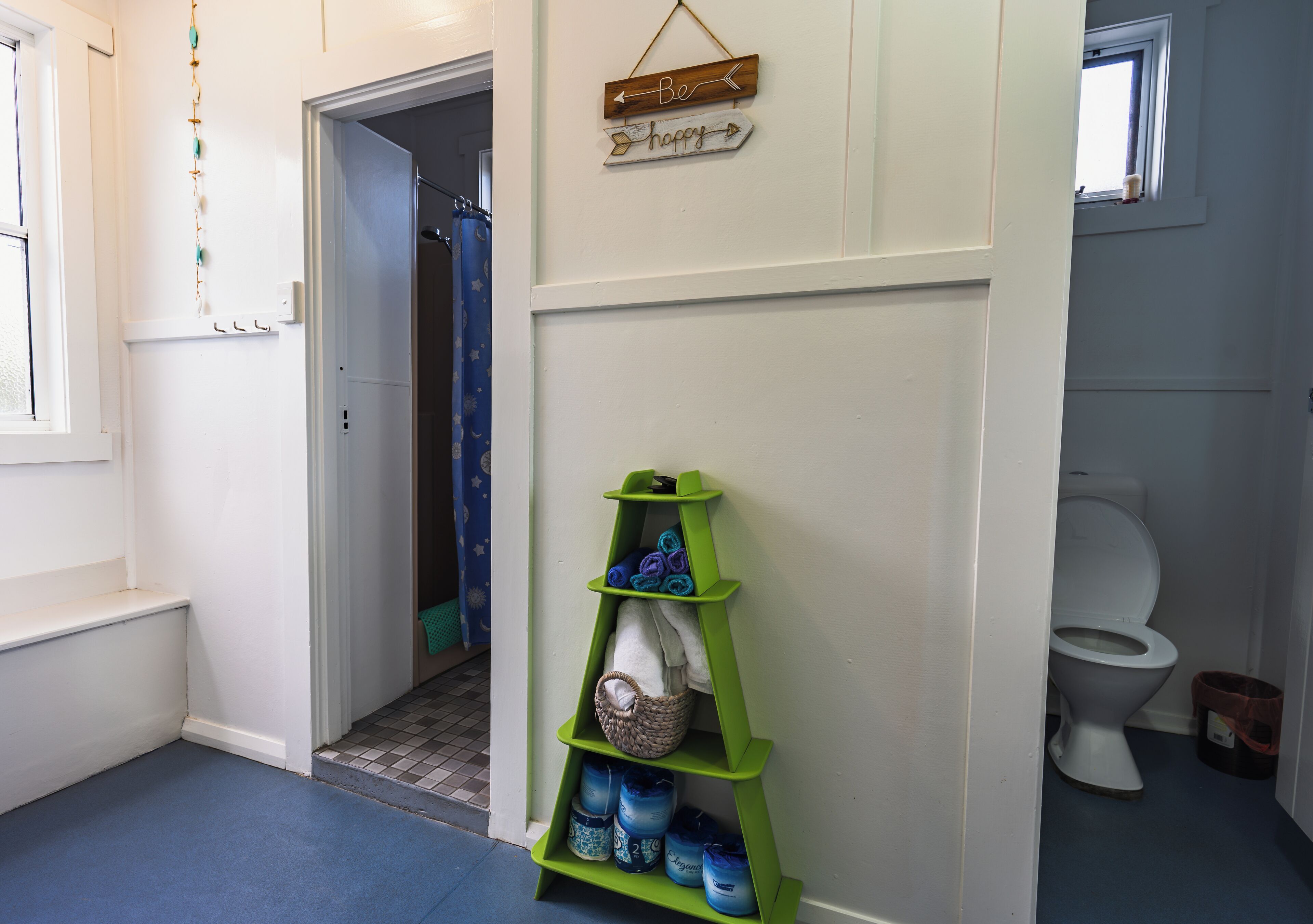 Un baño con un estante verde que contiene artículos de tocador, una cortina de ducha y un letrero en la pared.
