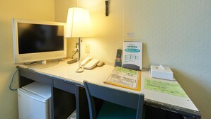 Ein Schreibtisch im Hotelzimmer mit einem Computermonitor, Telefon, Lampe und einer Fernbedienung an der Wand.