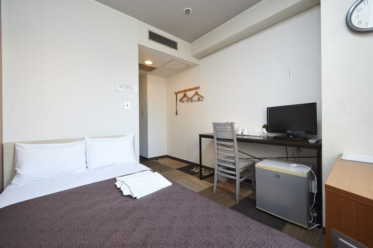 A hotel room with a bed, a desk with a computer, a TV, and a small refrigerator.