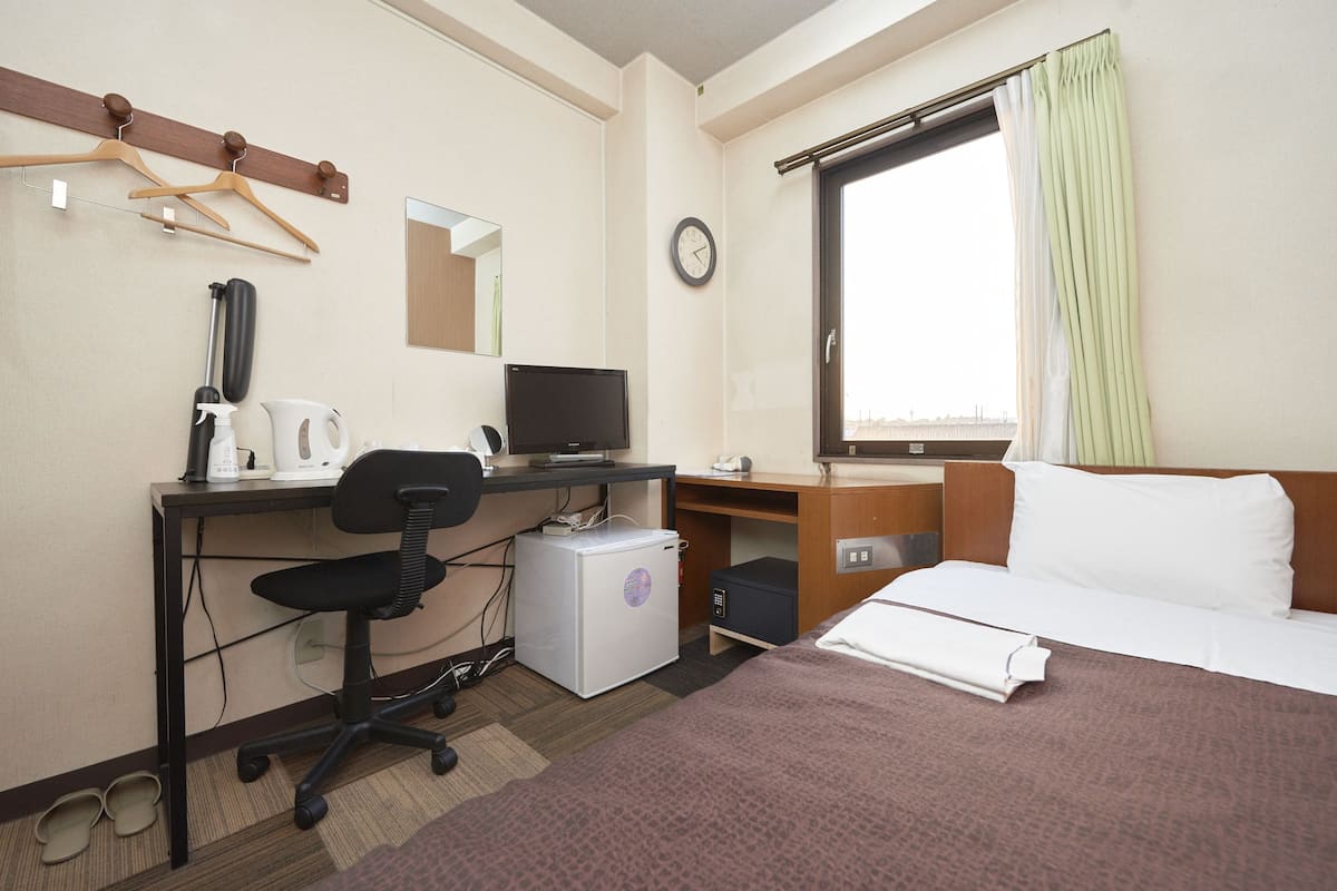 A hotel room with a bed, desk, chair, computer, and a small refrigerator.