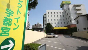 A yellow sign with green text and an arrow pointing right, indicating a direction. A white building with multiple windows and balconies is visible in the background. - Hotel Select Inn Utsunomiya (Utsunomiya)