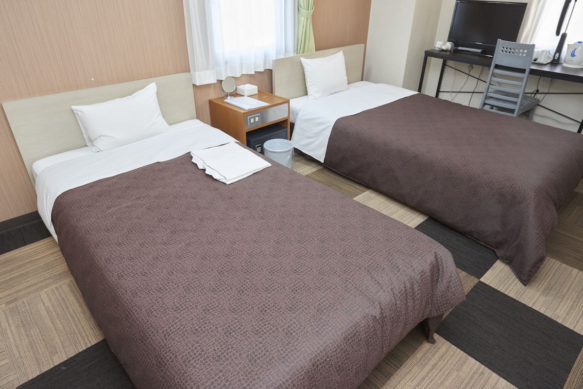 A hotel room with two beds, a desk with a computer, and a TV.
