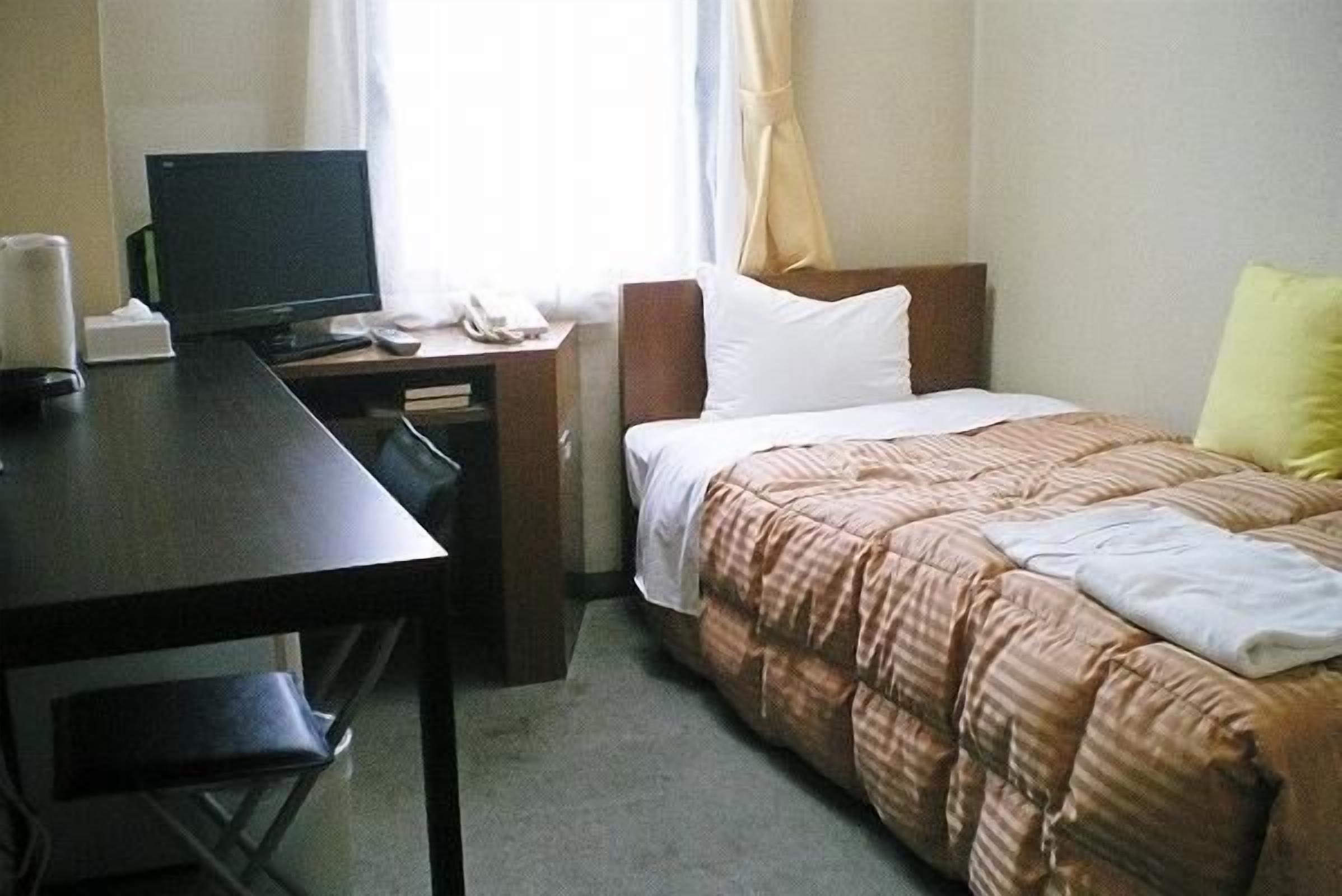 Una camera d'albergo con un letto, una scrivania con un computer e una sedia.