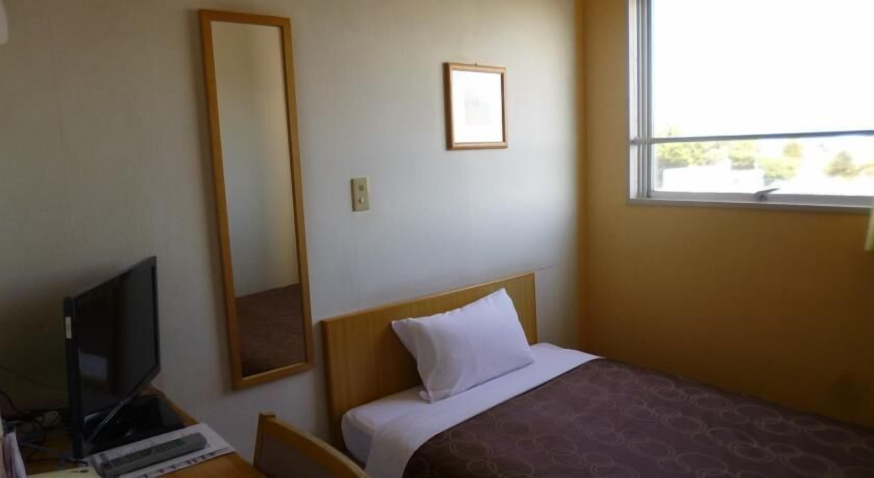 Una habitación de hotel con una cama, un escritorio con ordenador, un espejo y una ventana.
