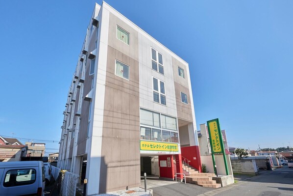 A modern building with a flat facade, large windows, and a visible entrance with a red door. - Hotel Select Inn Sano Ekimae (Sano)