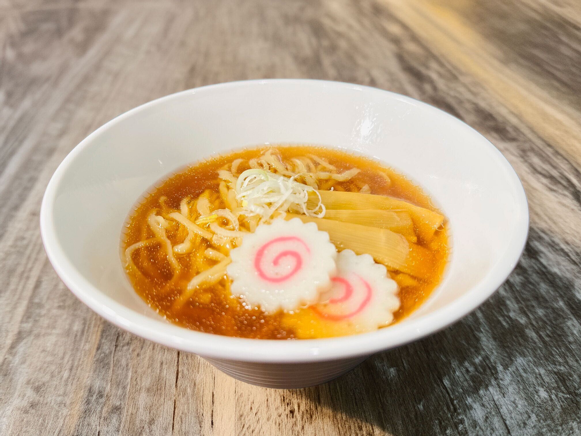 Een kom ramen noedels, bouillon en toppings op een houten tafel.