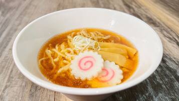 Een kom ramen noedels, bouillon en toppings op een houten tafel.
