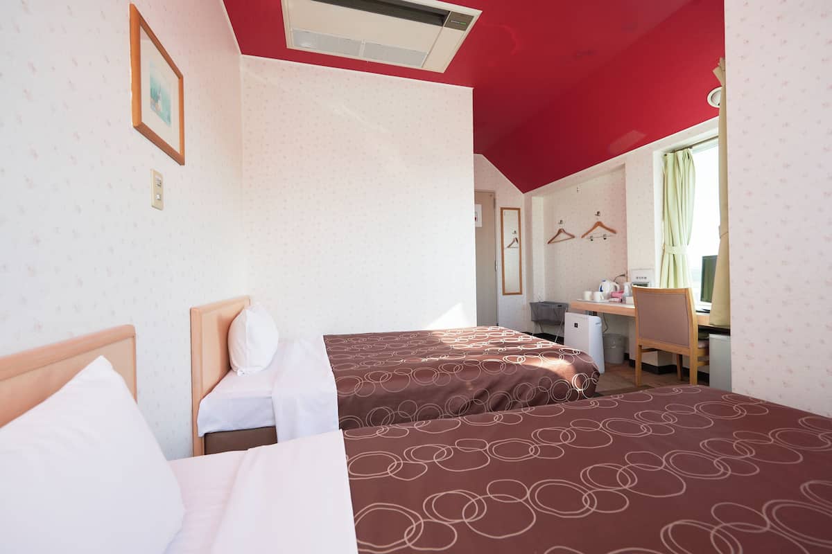 Quarto de hotel com duas camas, uma escrivaninha e uma cadeira.