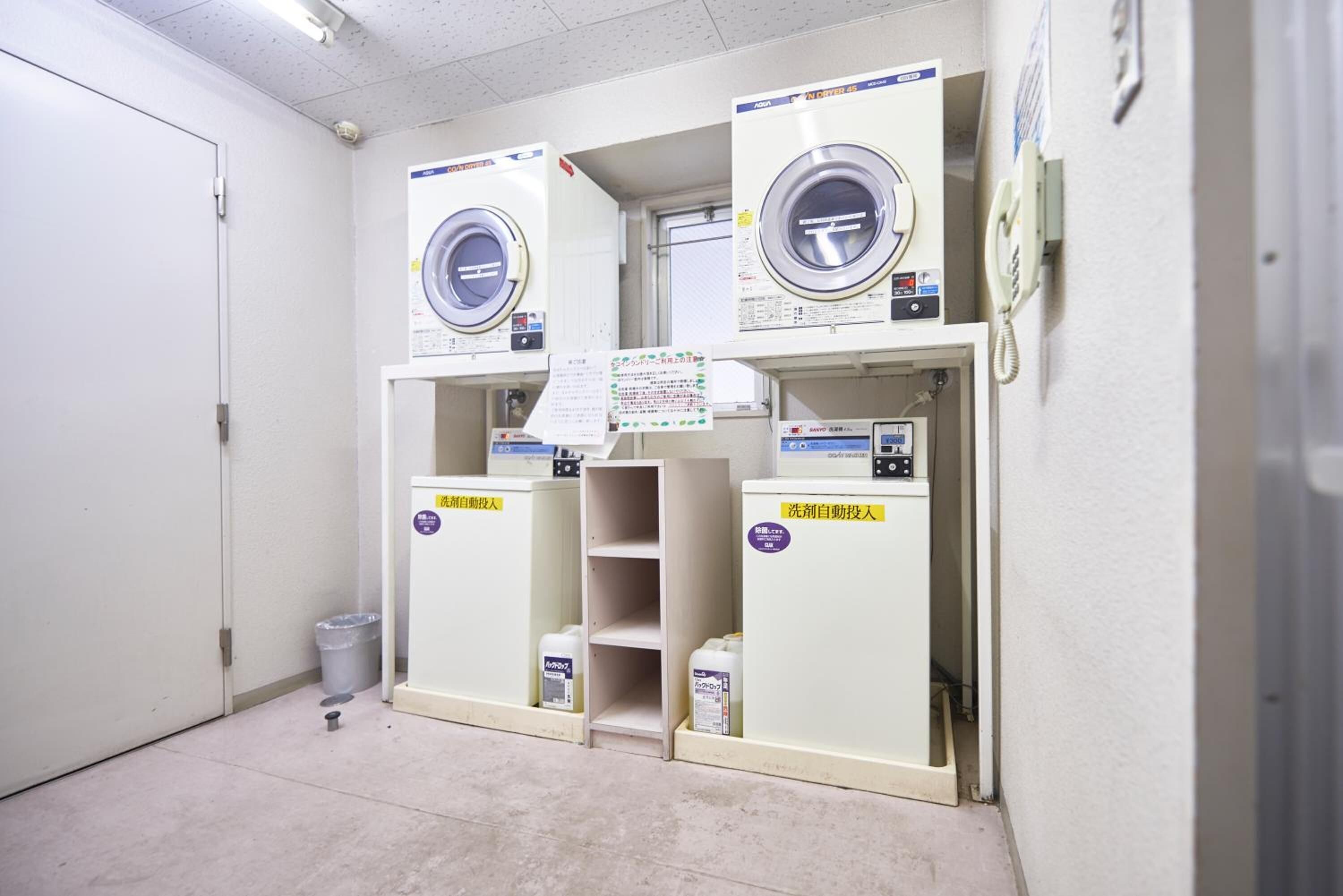 A laundry facility with three washing machines and a trash bin.