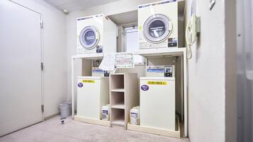 A laundry facility with three washing machines and a trash bin.