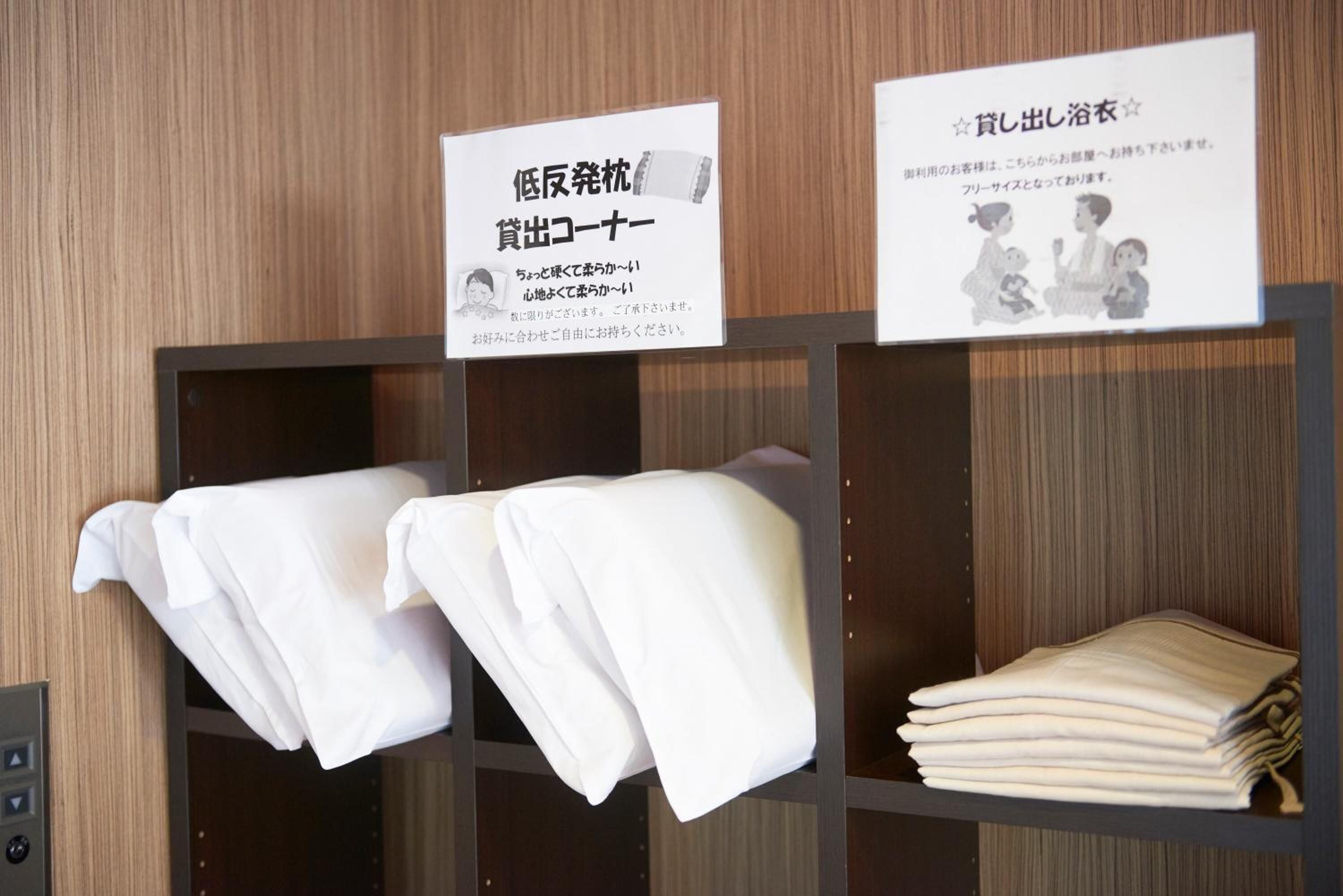 A hotel room with neatly folded white towels on a shelf and a signboard with Japanese text.