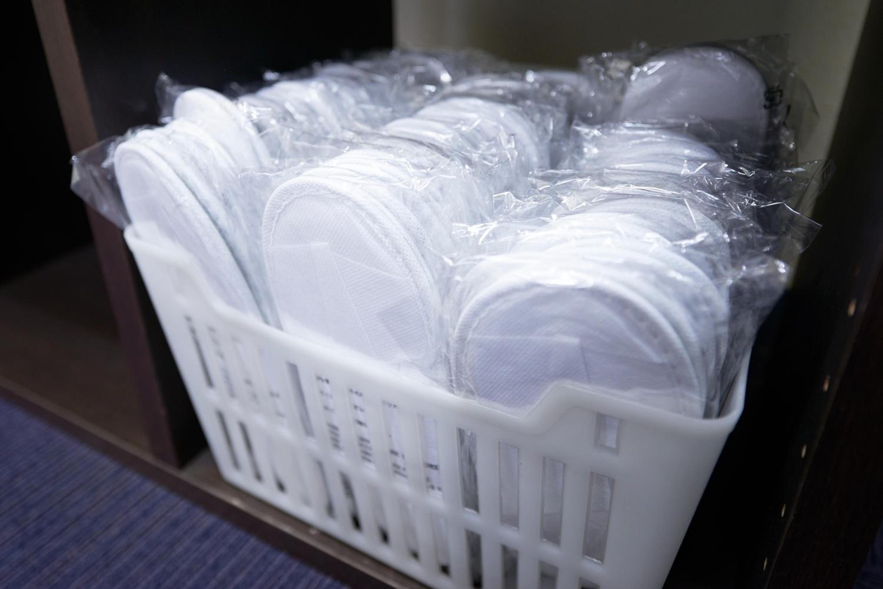 A white plastic basket filled with white circular objects, likely personal care items, stored in a room with a dark floor and a white wall.