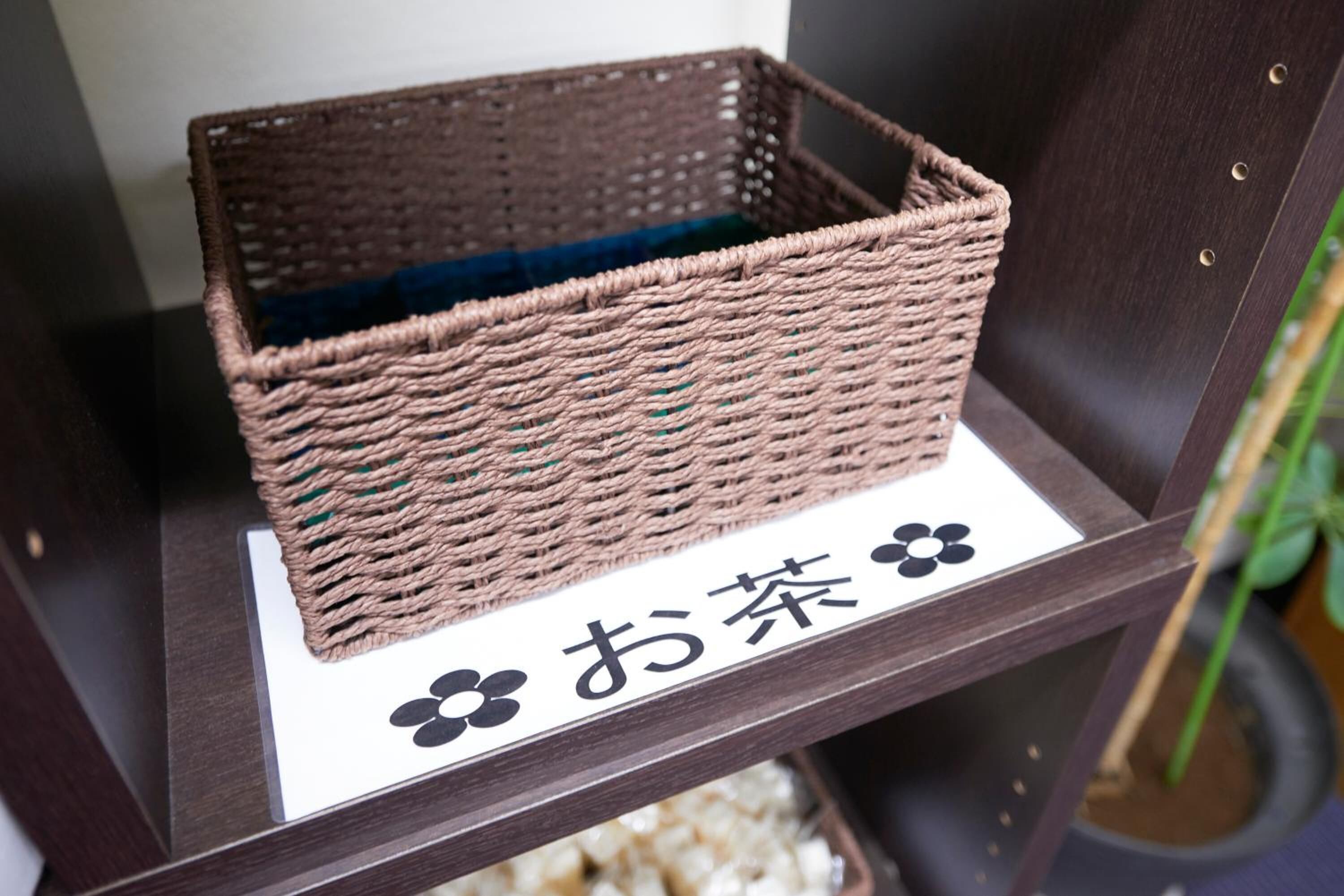 A wicker basket on a dark wooden shelf with a white label featuring Japanese characters and a black paw print.