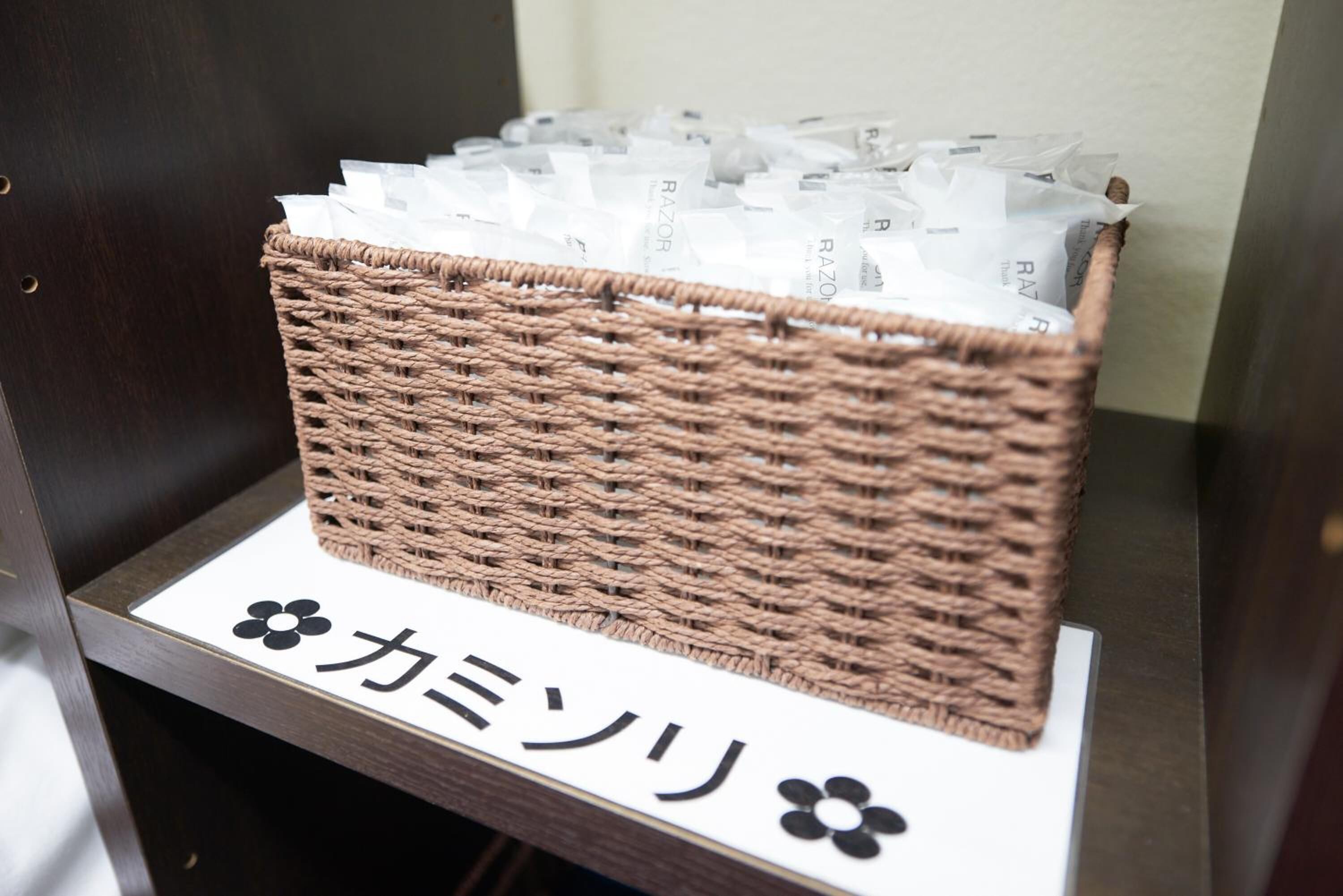 Una cesta de mimbre llena de sobres blancos sobre un soporte de madera con un letrero que dice 'カミソリ'.