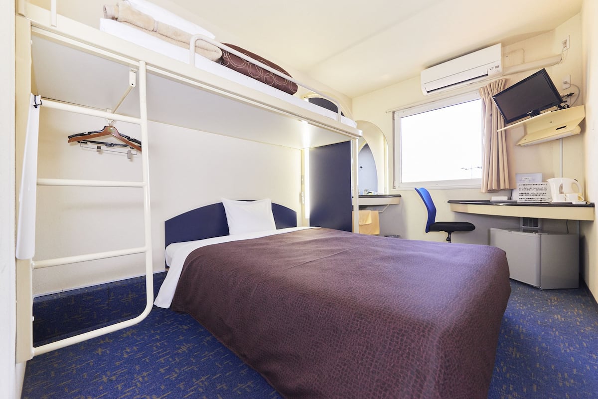 A compact hotel room with a bunk bed, a desk with a computer, and a small kitchenette.