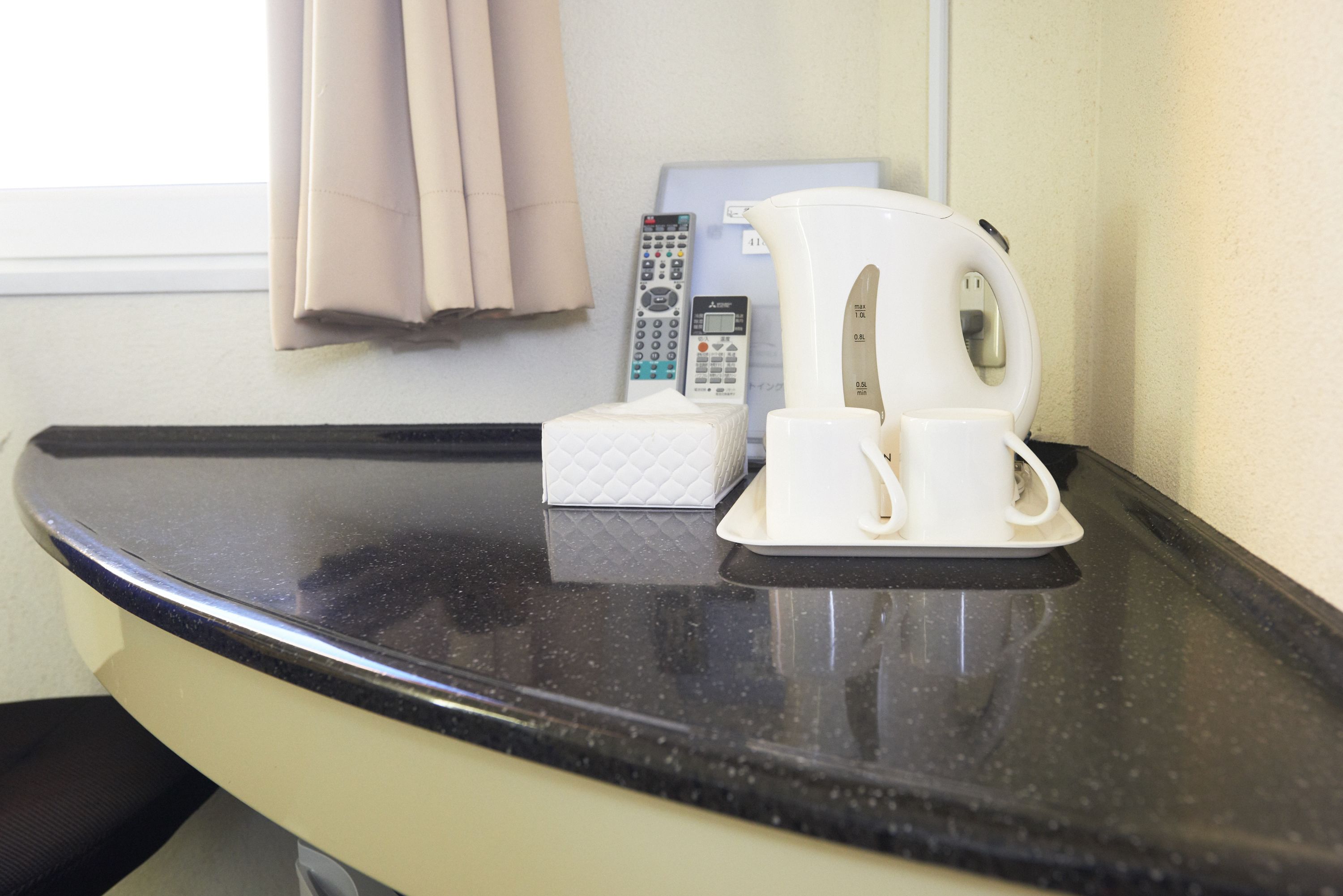 A countertop with a coffee maker, a tissue box, and a remote control.