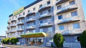Ein mehrstöckiges Hotel mit Balkonen, einem Restaurant im Erdgeschoss und einem Parkplatz.