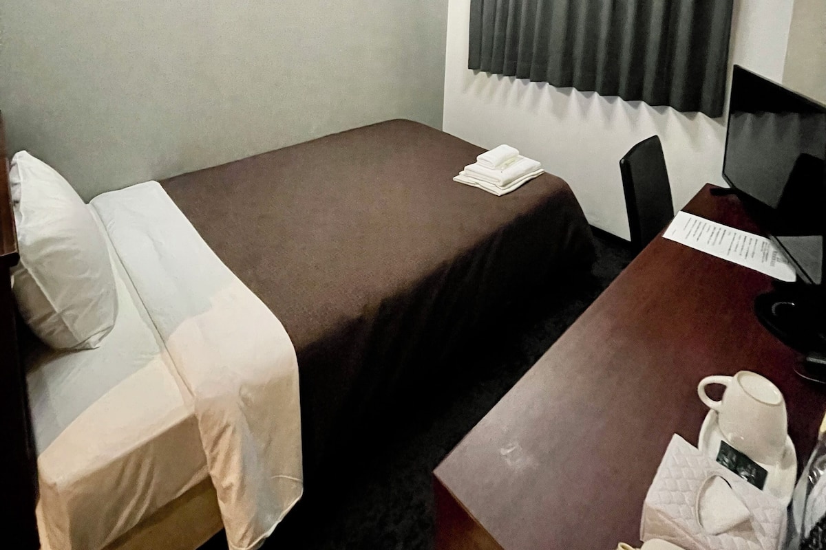 A hotel room with two single beds, a desk with a computer, a chair, a telephone, and a window with curtains.