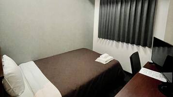 A hotel room with two single beds, a desk with a computer, a chair, a telephone, and a window with curtains.