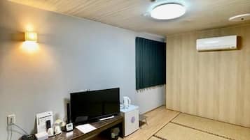 Una habitación con una televisión de pantalla plana, un mueble de entretenimiento de madera, un aire acondicionado de pared y suelo de este tipo de alfombra tradicional japonesa.