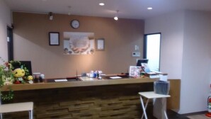 A reception desk with a clock, framed pictures, and a small plant. - Hotel Select Inn Saitama Moroyama (Moroyama)