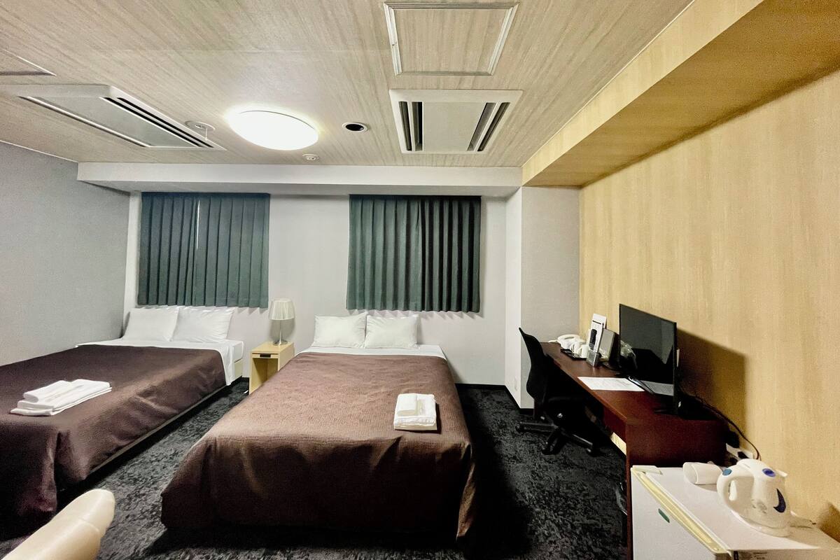 A hotel room with two beds, a desk, a chair, a TV, and a desk lamp.
