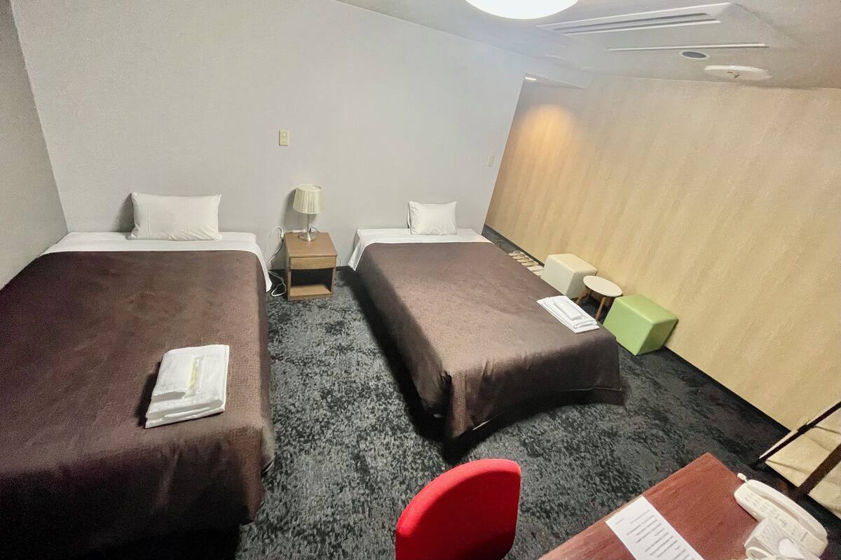 A hotel room with two beds, a desk, a chair, a lamp, and a telephone.