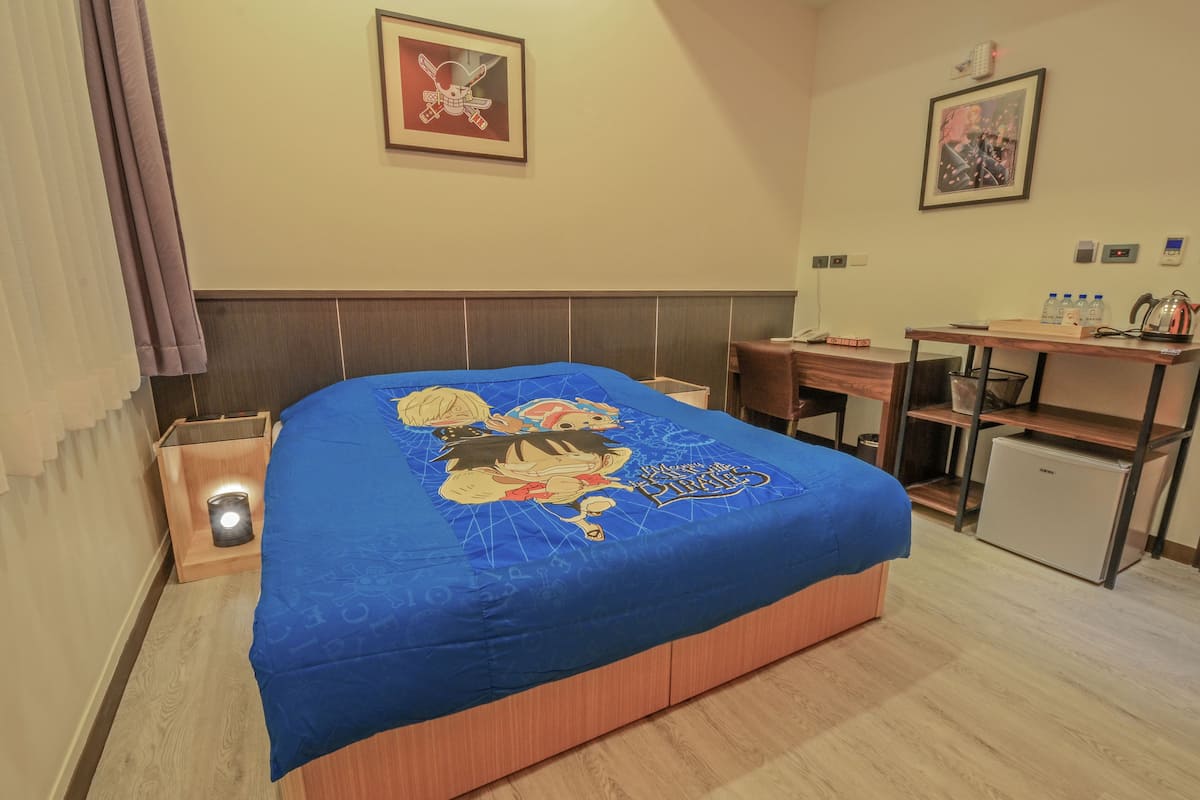 Une chambre d’hôtel avec un lit décoré d’un motif de personnage de dessin animé, un bureau avec une bouilloire et un petit réfrigérateur.