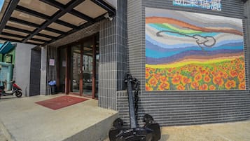A building entrance with a tiled wall, a red mat, and a scooter parked outside.