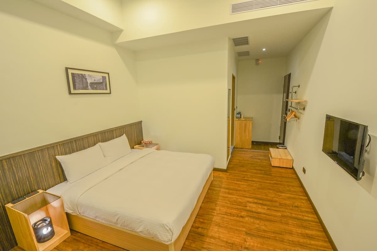 Une chambre d’hôtel avec un lit, une table de chevet, une télévision et un plancher en bois.