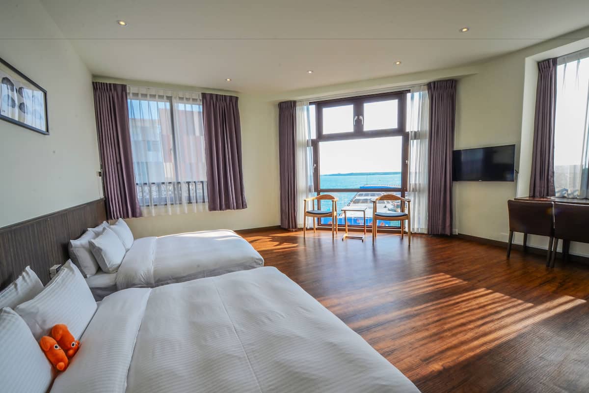 Une chambre d’hôtel avec deux lits, un bureau et vue sur la mer.