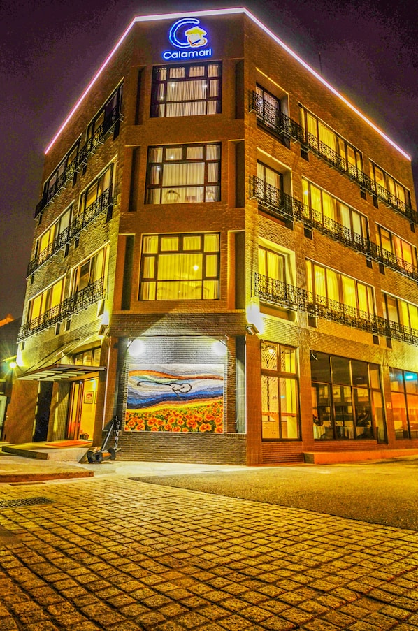 A multi-story hotel with a prominent sign at the top, large windows on each floor, and a visible entrance with a ramp.