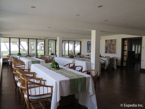 Un comedor con mesas y sillas largas, ventanas amplias y obras de arte en las paredes.