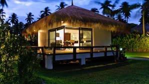 A thatched-roof bungalow with a glass-enclosed veranda, surrounded by lush greenery and palm trees. - Hijo Resorts Davao (Tagum)
