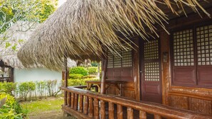 A traditional wooden house with a thatched roof, a wooden porch, and a view of a garden. - Hijo Resorts Davao (Tagum)