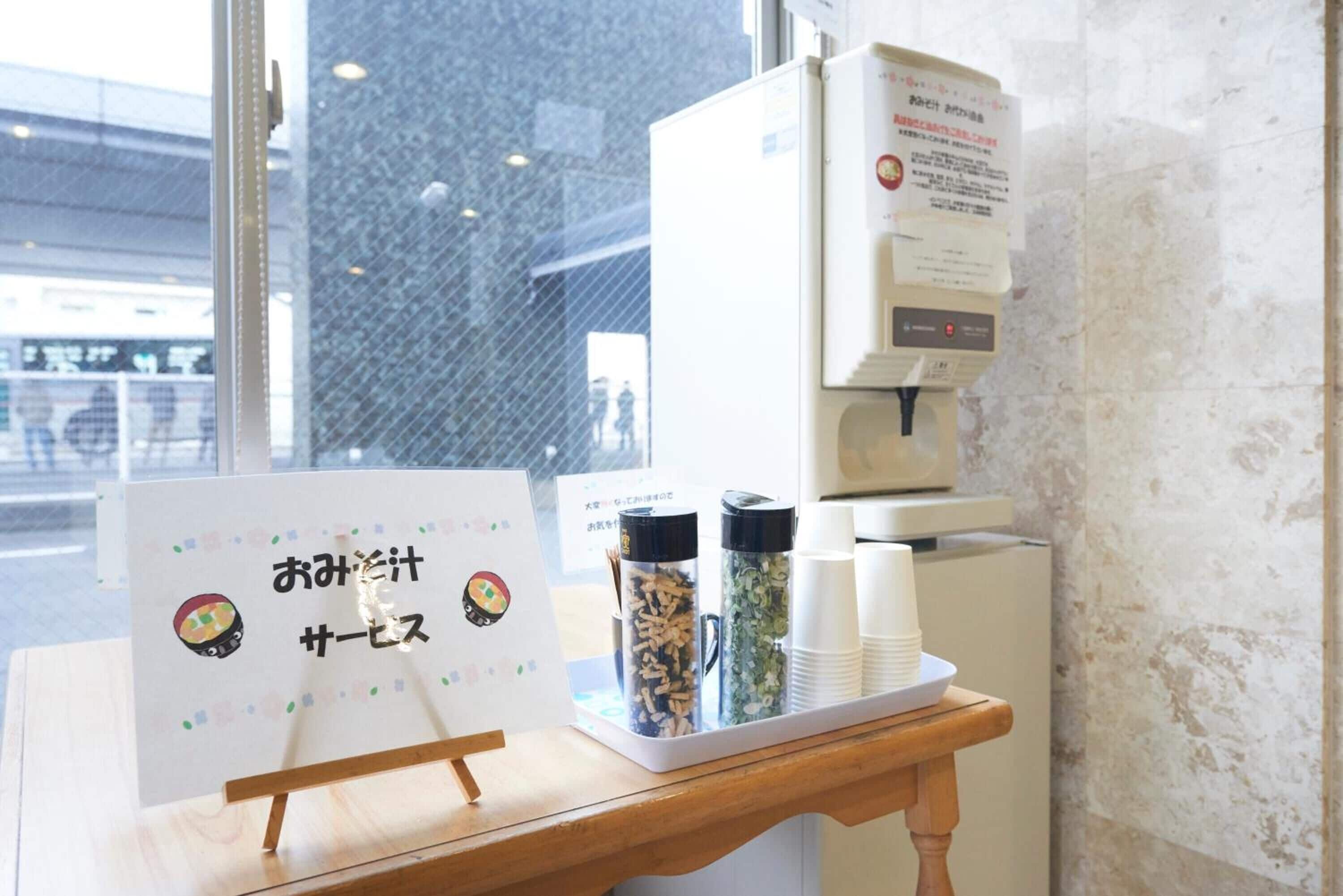 Una estación de café con un tablero de menú, dispensadores de café y un recipiente de vidrio con granos de café.