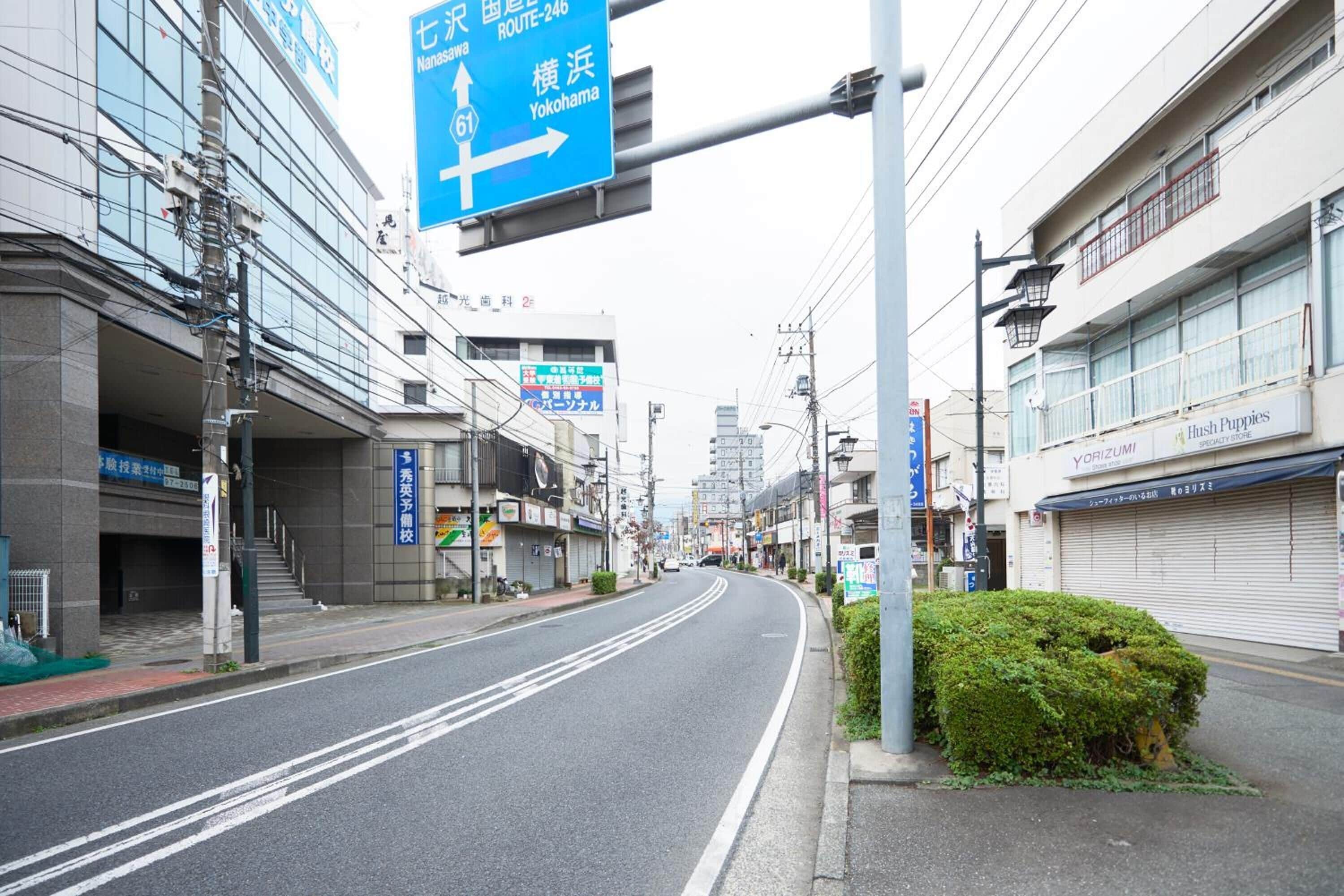 A street with a blue directional sign, buildings, and a bush.