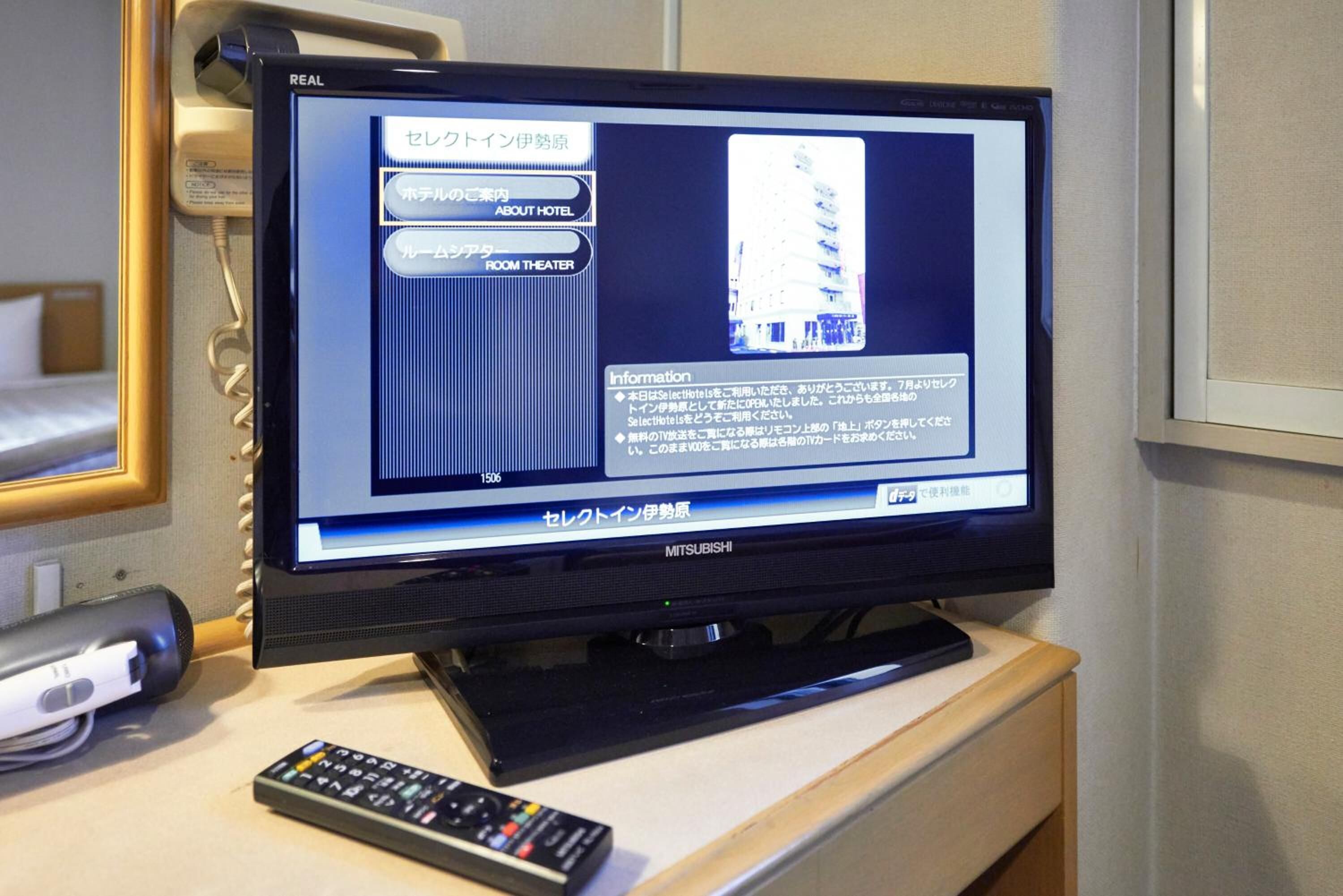 A television displaying hotel information in Japanese, with a remote control on a wooden surface beside it.