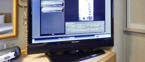 Een televisie toont hotelinformatie in het Japans, met een afstandsbediening op een houten oppervlak ernaast.