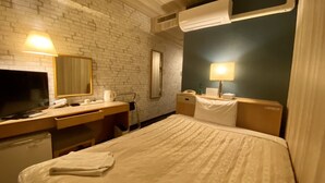 A hotel room with a brick wall, a flat-screen TV, a desk with a telephone, a bedside table with a lamp, and a bed with a white comforter. - Hotel Select Inn Isehara (Isehara)