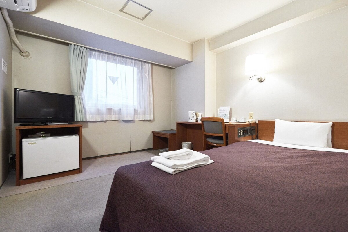 Une chambre d’hôtel équipée d’un lit, d’un bureau, d’une télévision, d’une machine à café et d’un téléphone.
