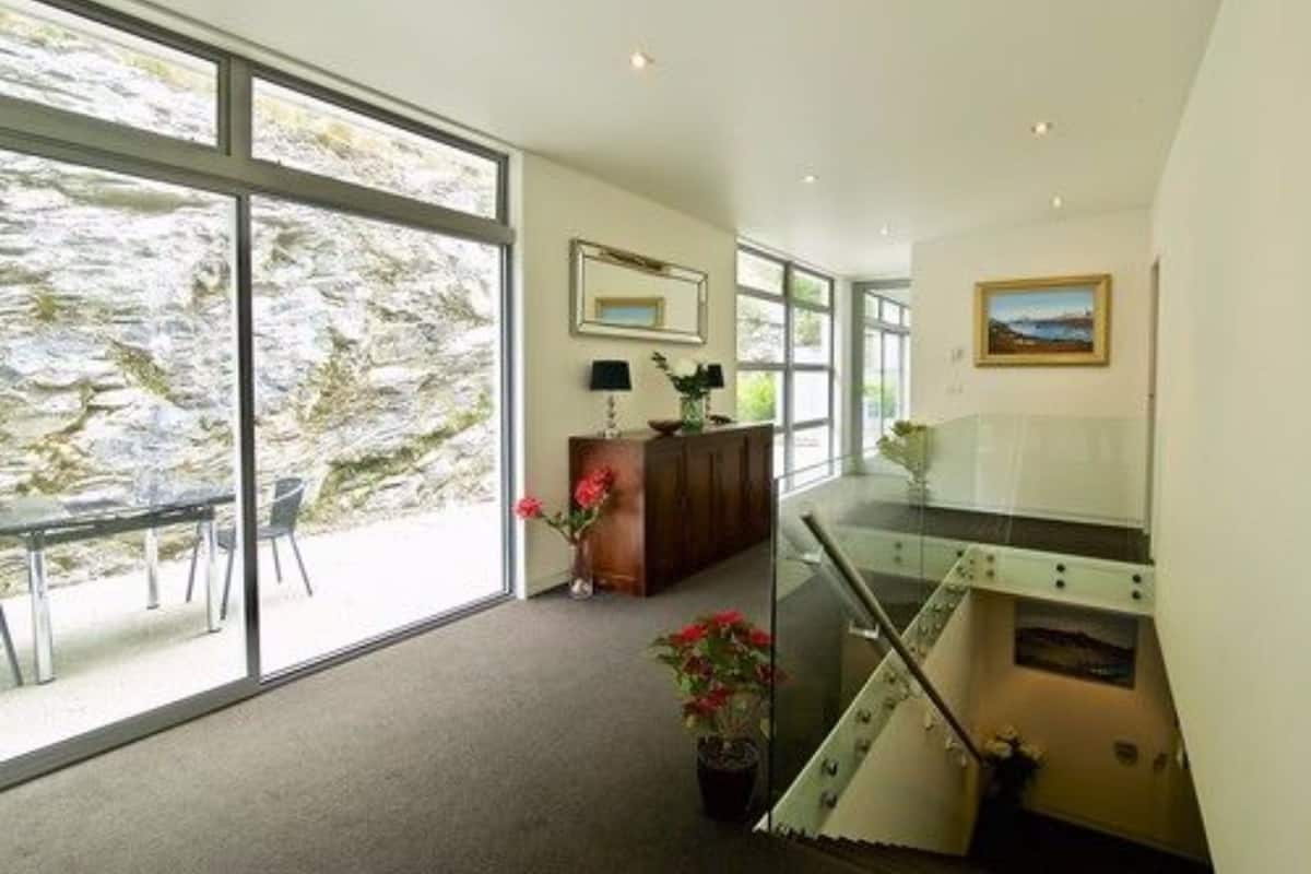 A spacious room with large windows, a wooden cabinet, and a staircase.