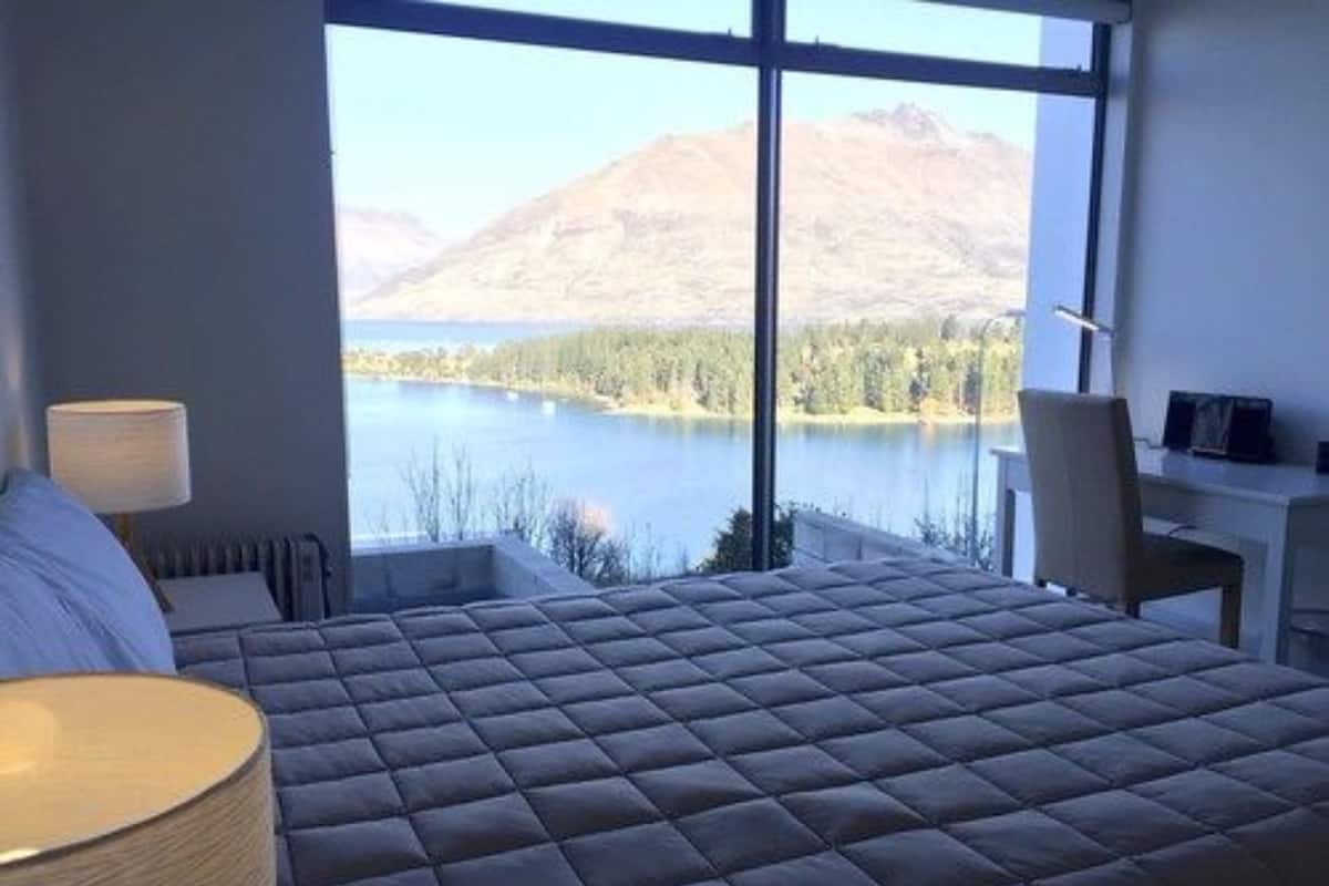A bedroom with a large window offering a view of a lake and mountains.