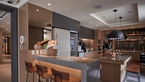 A modern kitchen with a central island, bar stools, a refrigerator, and a hanging pendant light.